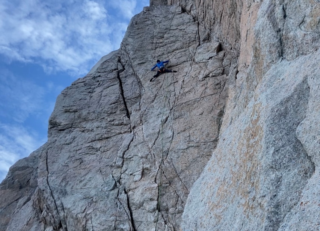 Climber delicately climbing the technical face of the pink granite rock which has lots of cracks and features in at Gullnausen