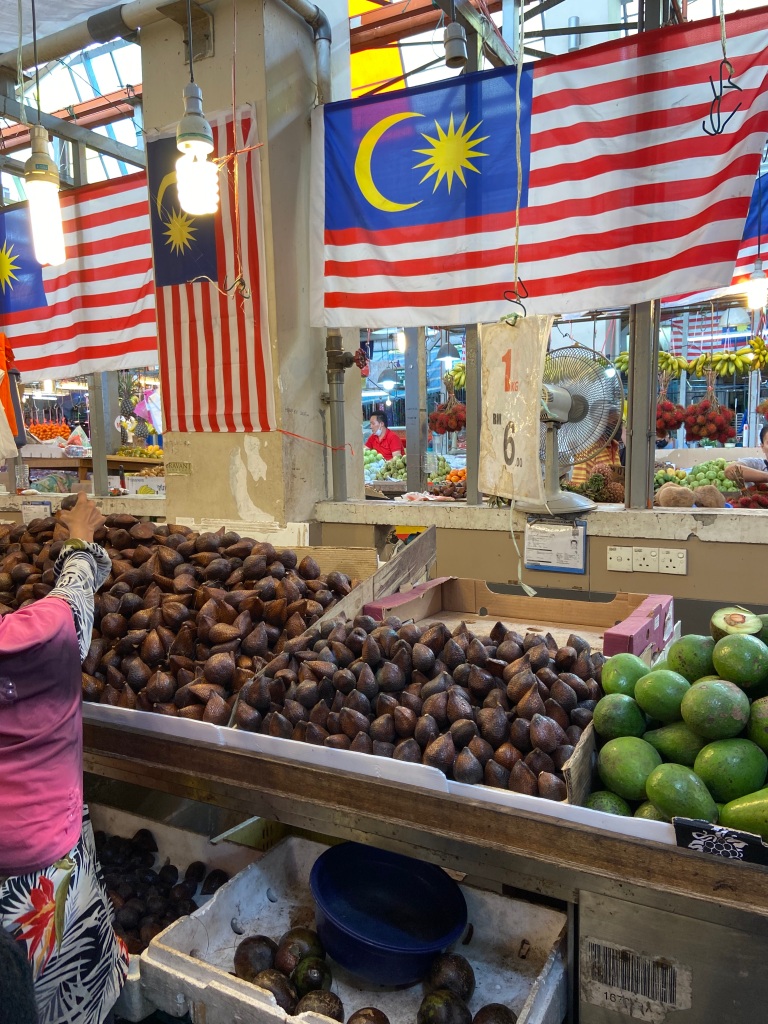 Piles of exotic fruit at the Chow Kit  market in Kuala Lumpur with the Malaysian flags behind.