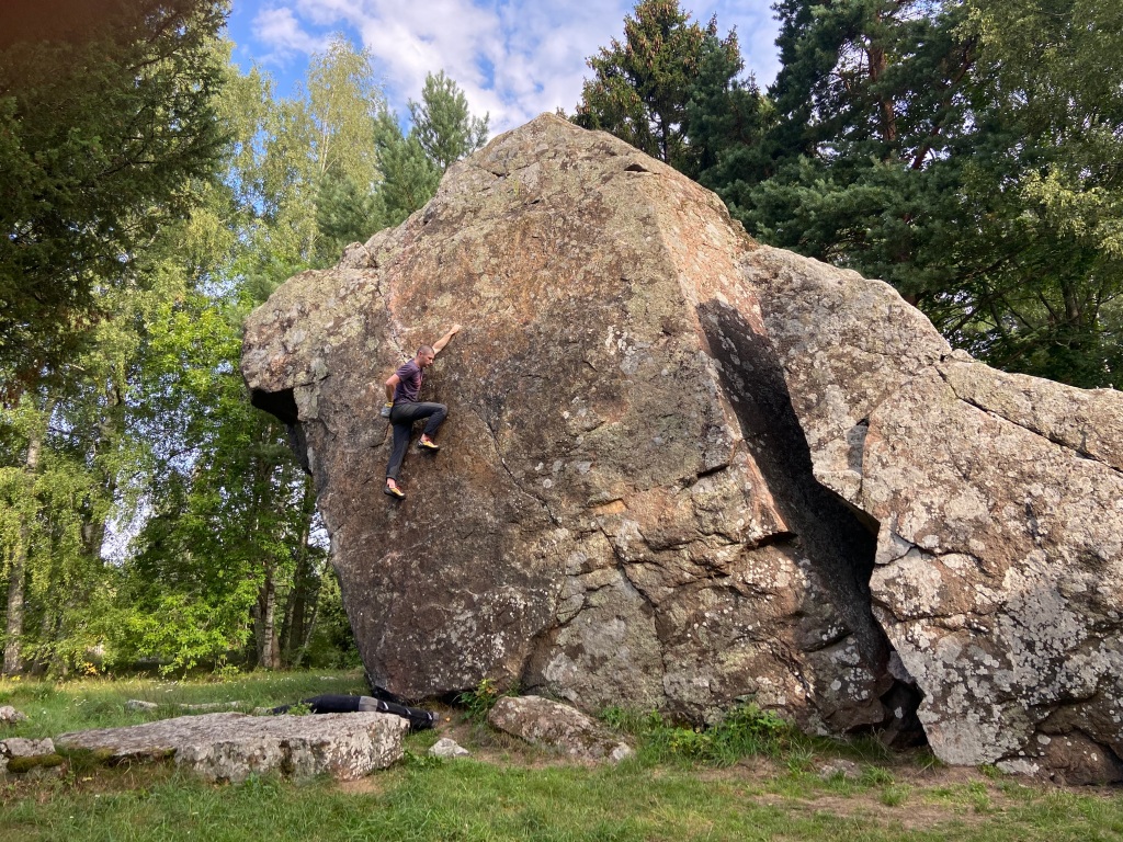 Climber on large boulder with a flat grass landing with rocks