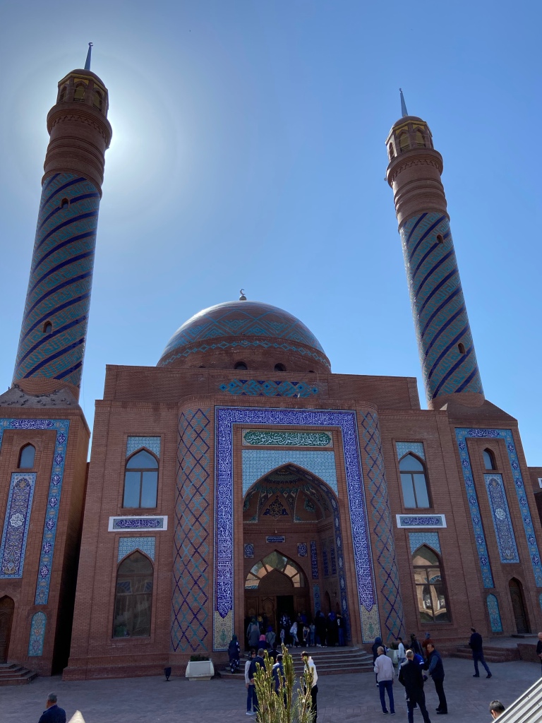 Red brick mosque which is covered in  ornate cobalt blue tiles around the two minarets on either side of the building and around the tall and grand entrance way. The dome at the top is decorated with pale blue tiles and is adorned with a crescent moon 