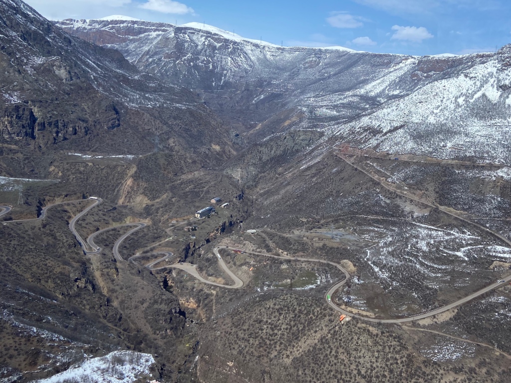 A deep gorge surrounded with snowy mountains, with a narrow road winding through with lots of hairpin bends. 
